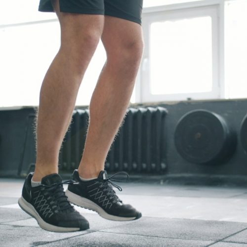 Tilt-up of sporty man jumping with skipping rope in gym working out alone busy with cardio exercise. Healthy lifestyle, people and active youth concept.