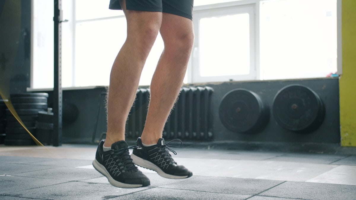 Tilt-up of sporty man jumping with skipping rope in gym working out alone busy with cardio exercise. Healthy lifestyle, people and active youth concept.
